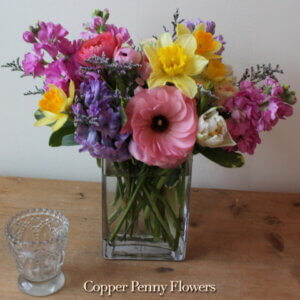 Come Spring flower arrangement featuring stock, daffodils, and ranunuculus in pinks and yellows and purples