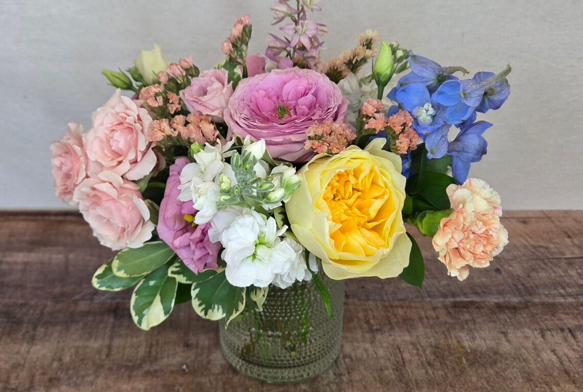 Afternoon Tea is a mixed pastel arangement featuring roses and delphinium with greenery in a beaded glass vase