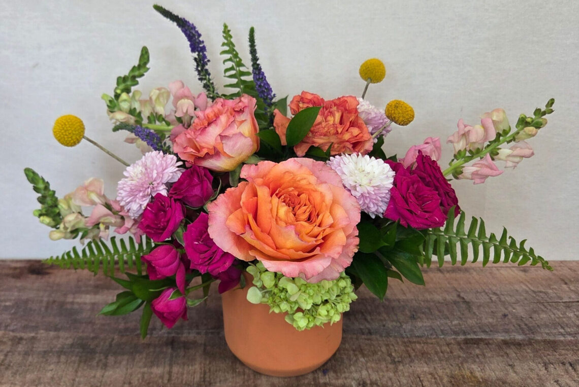 Apricot Smoothie is a cheerful arrangement with orangey apricot roses, hot pink spray roses, pastel snap dragons, and yellow Billy balls in a pastel container
