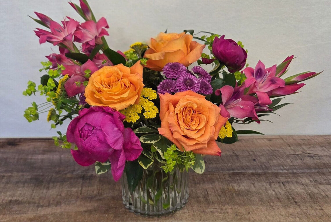 Bloomin' Bohemian is a hot pink and orange arrangement featuring roses and peonies in a glass vase.