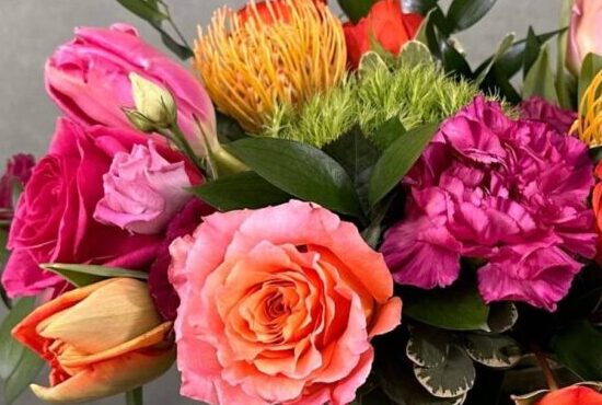 Color Me Rosy is a festive mix of bright orange and hot pink bloos in a glass leaf-lined vase