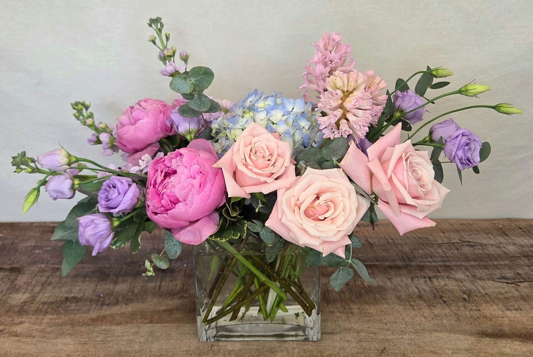 Cape Horizon is a pastel arrngement in a glass vase featuring light pik roses and darker pink peonies with blue and lavender accents