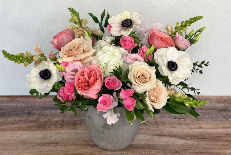 Charming Blush is a pink, blush, and white arrangement featuring roses and anemones in a rustic container