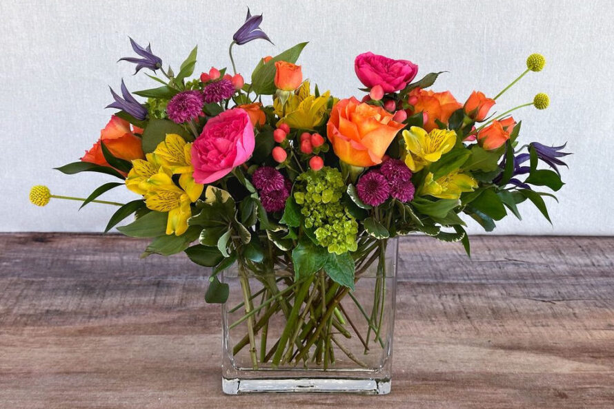 Color Me Joy is a bright mix of orange, hot pink, green, yellow, and purple blooms in a glass container