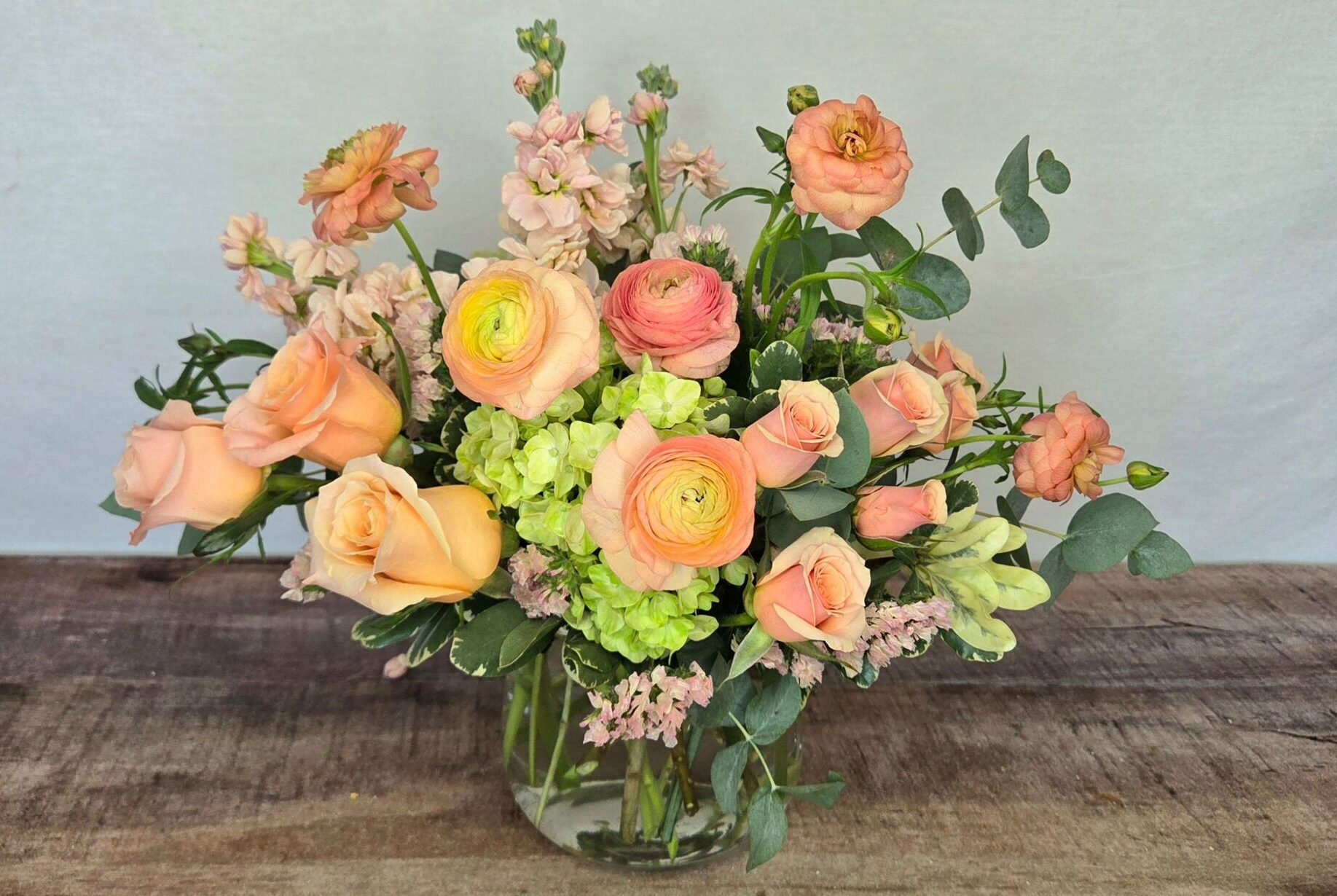 Golden Hour is a peach and mint green arrangement featuring ranunculus in a glass vase