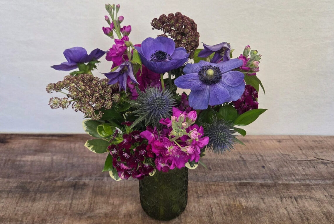 Grape Jam is a mix of magenta and purple blooms featuring stock and anemone in a colored-glass container