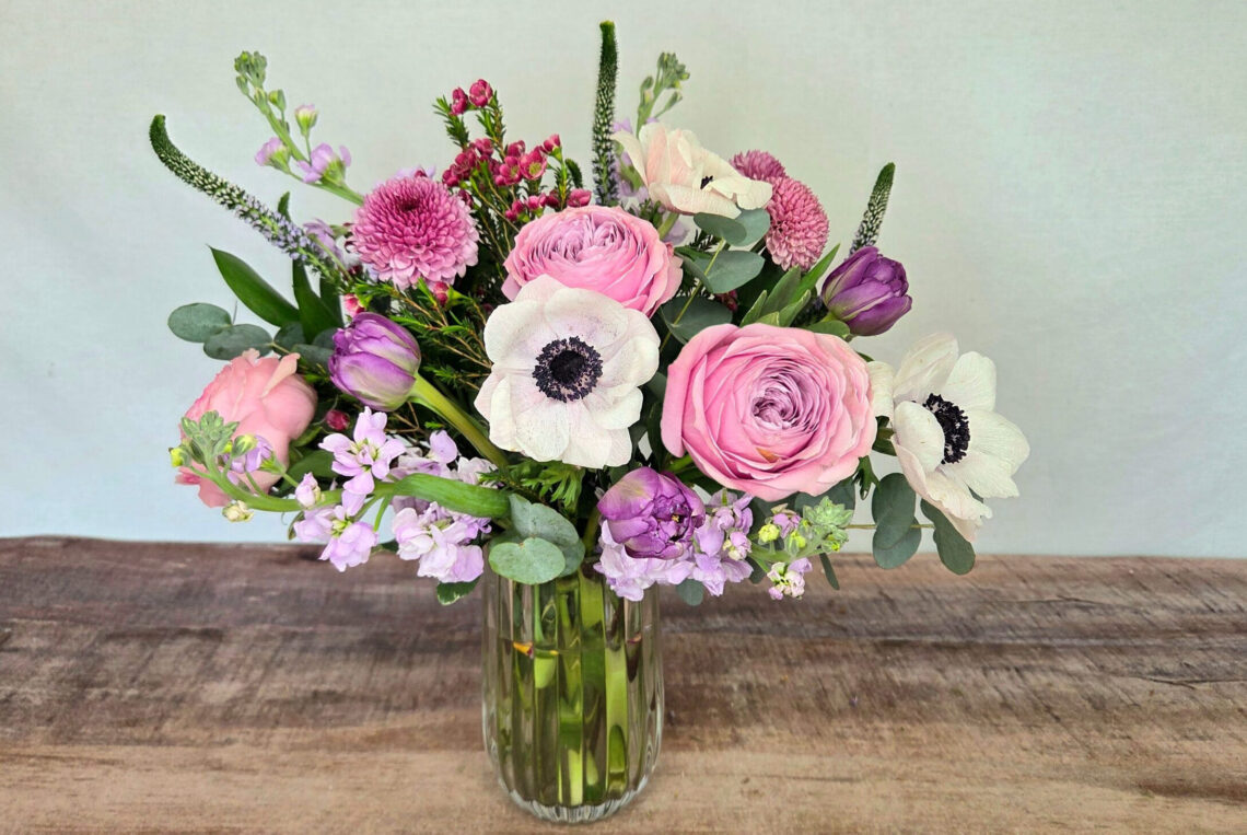 Lavender Waltz is lavender, pink, and white premium blooms featuring white anemone and pink ranunculus in a glass vase