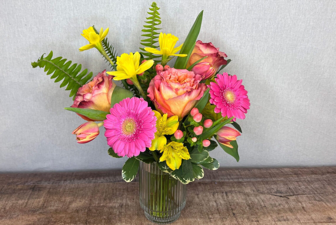 Sunshiny Day is bright yellow tulips with hot pink Gerbera daisies and orange roses in a decorative glass vase