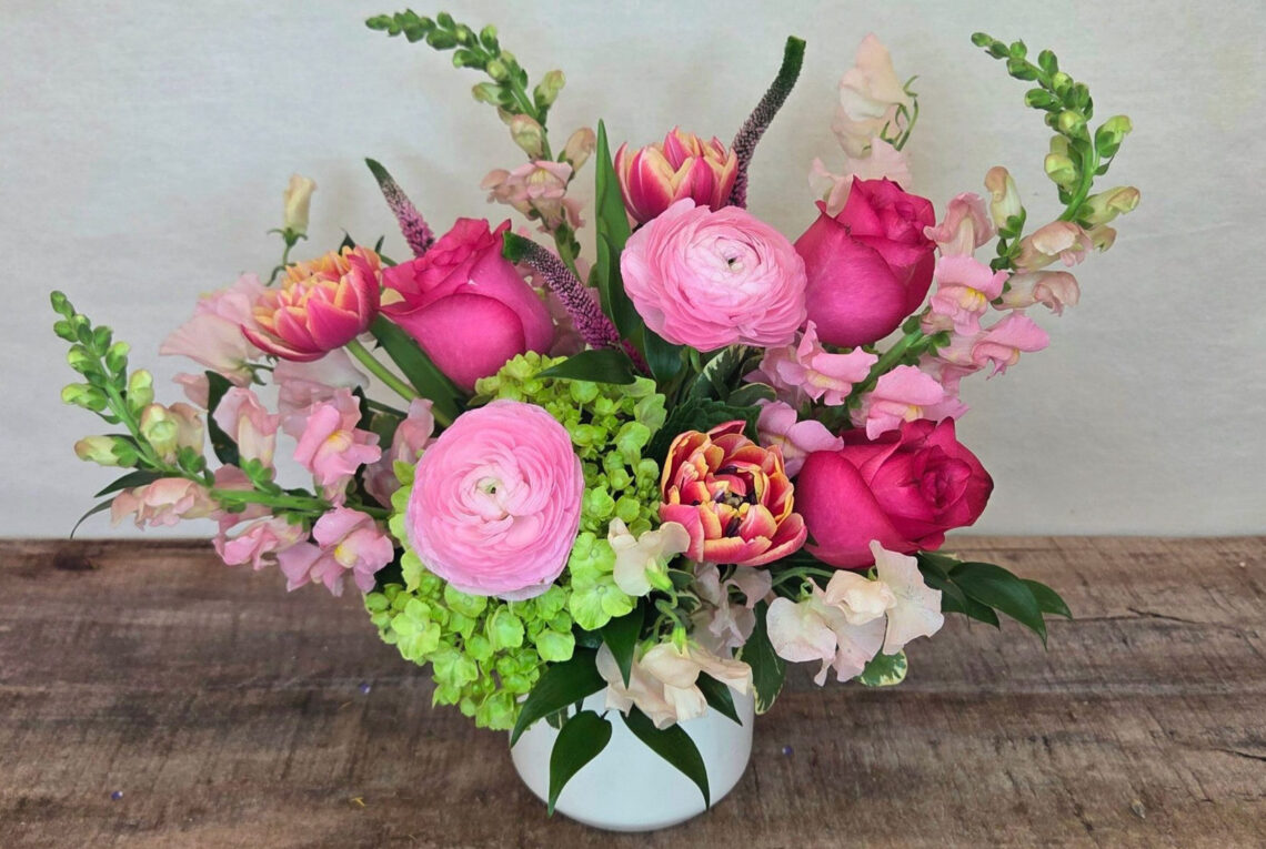 Sassy Sorbet is a cheerful mix of hot pink roses, pink ranunculus, and green hydrangea with tulips and pink snap dragons in a white container
