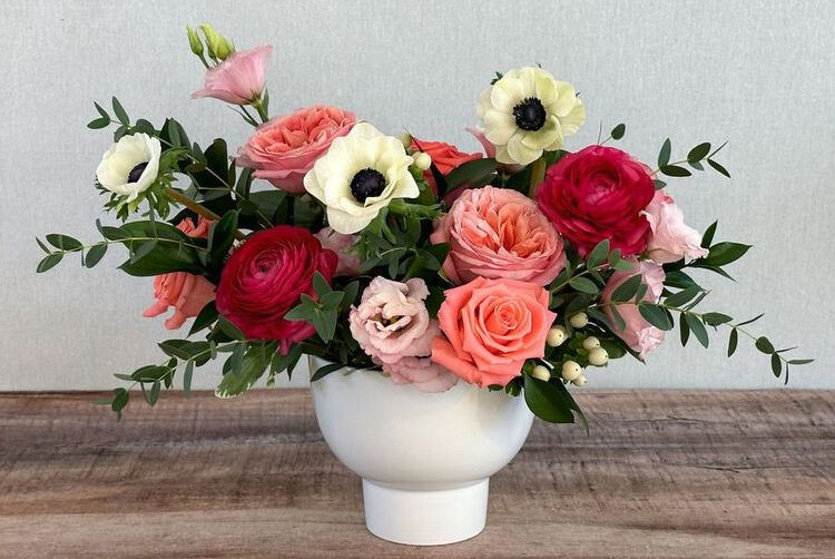 Still The One is an elegant mix of roses, ranunculus, and panda anemones with premium greens in a footed white vase