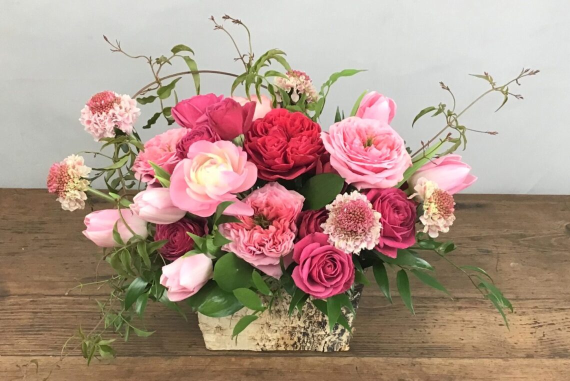 Sugar Pie is all shade of pink featuring roses and ranunculus in a birth container
