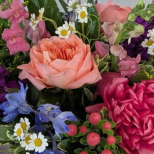 Bloomin' Parade os a bright mixed color flower arrangement featuring roses, peonies, stock, and snapdragon in a leaf-lined glass vase