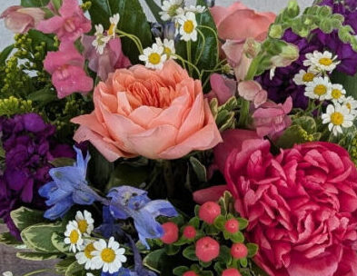 Bloomin' Parade os a bright mixed color flower arrangement featuring roses, peonies, stock, and snapdragon in a leaf-lined glass vase